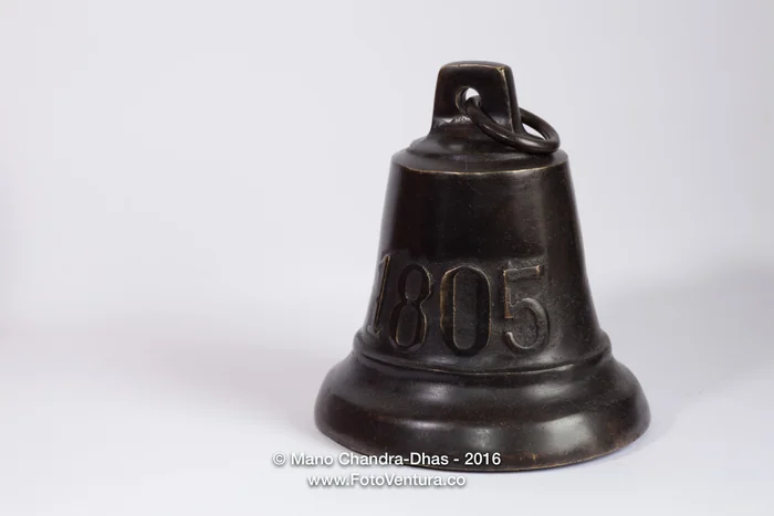 An antique bronze bell dated 1805 on a white background