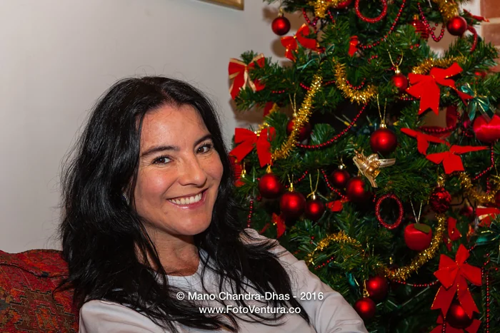 A smiling woman beside a decorated Christmas tree