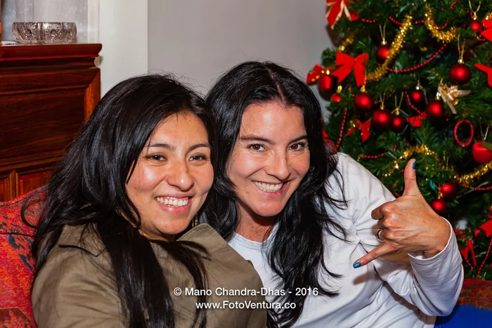 Two friends laughing together by a Christmas tree