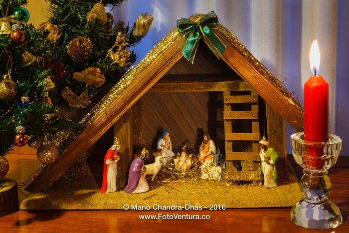A Christmas nativity crib beside a lit red candle