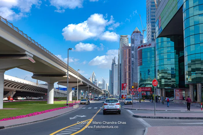 Dubai, United Arab Emirates - Elevated Railway Track To The Left And Modern Skyscrapers To The Right, Where Once Was Only Sand And A Desert Road; Road Markings In Foreground.