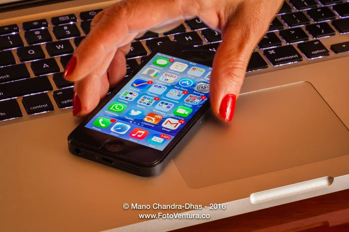 Latin lady's fingers picking up iPhone5 from computer keyboard; close-up