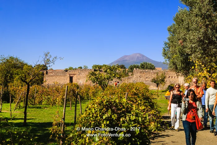 Italy - tourists walk through ruins of Pompeii, Vesuvius background.