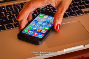 Latin lady's fingers picking up iPhone5 from computer keyboard;